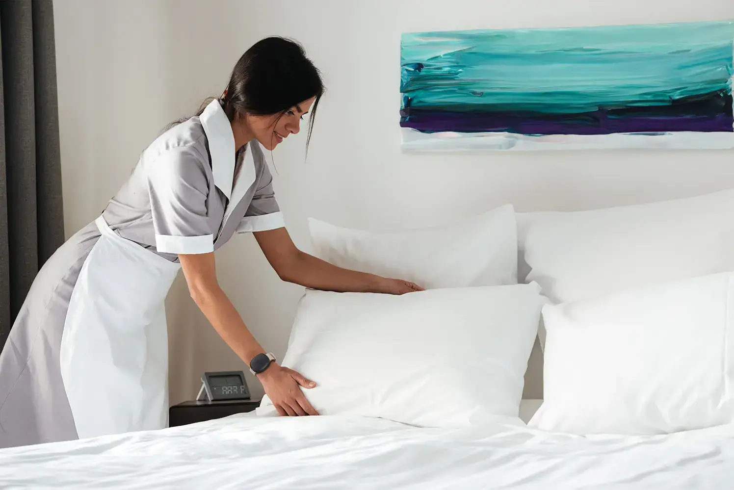 Hospitality - Housekeeper with Silent Beacon: Housekeeper in a hotel room wearing a Silent Beacon panic button for business for safety during room cleaning tasks.
