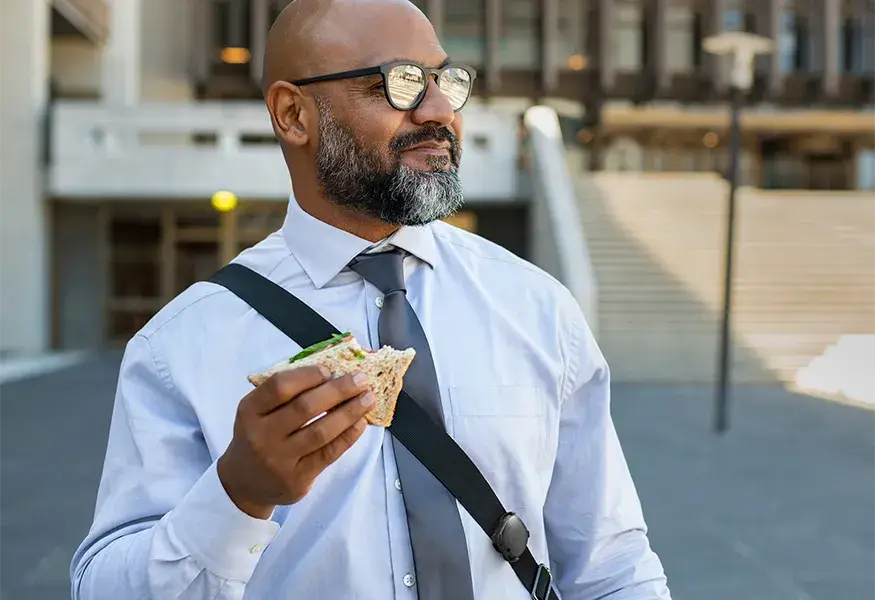 Man in sunglasses wearing eating a sandwich while wearing a beacon on his shoulder bag strap