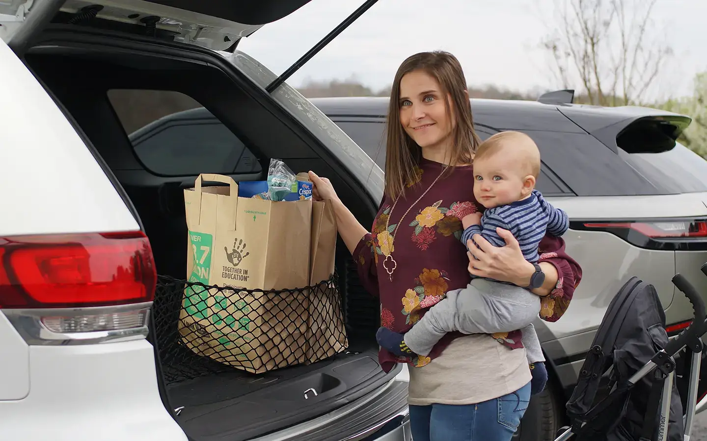 Woman wearing her Silent Beacon emergency call button while putting groceries in car and holding her baby.