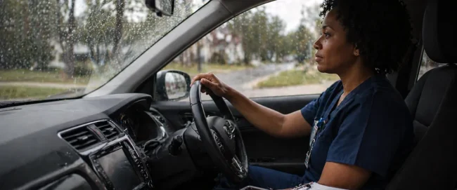 Home health nurse sitting in a car before a patient visit during rainy weather.